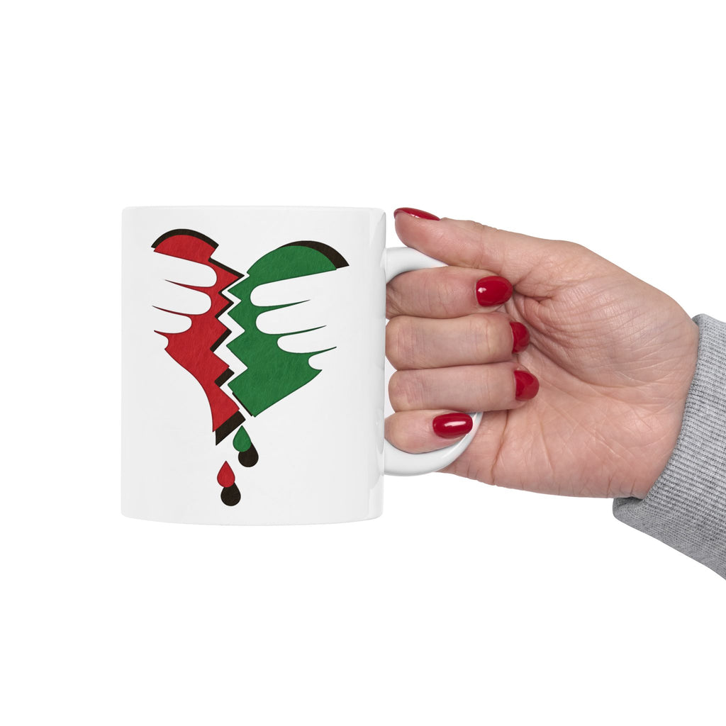 Broken Heart Palestine ceramic mug with a vivid red-green split heart motif, symbolizing solidarity, held by a hand.